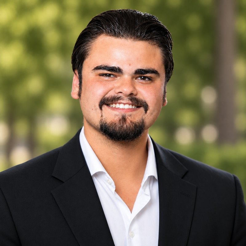 Kyle Andrew Ryan smiling outdoors, wearing a black jacket and white shirt.